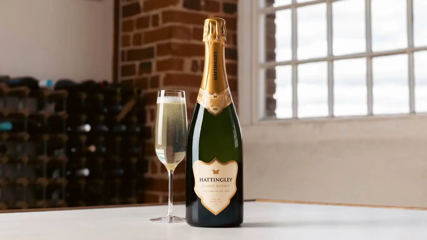 Titelseite -Weinhaus Shop Bottle of English sparkling wine next to a glass of English sparkling wine on a table in front of a window